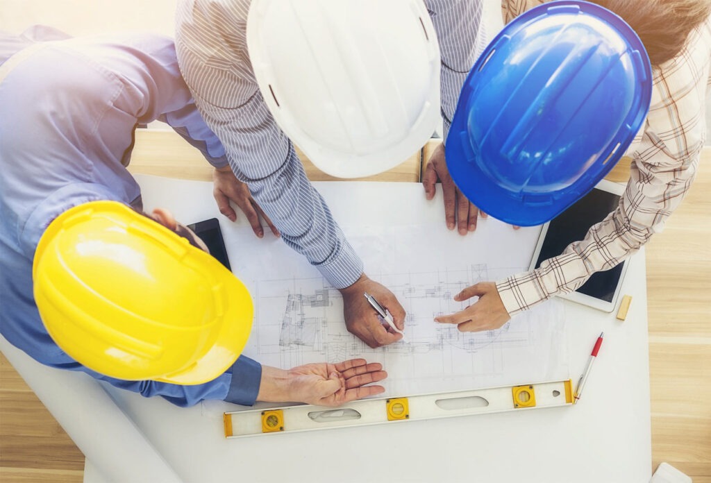 Construction professionals in hard hats collaboratively reviewing architectural plans on a table, highlighting teamwork in project planning.