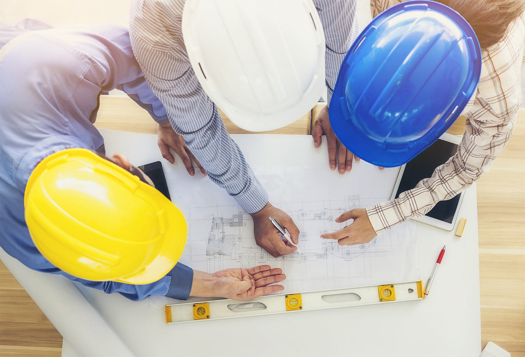 Construction professionals in hard hats collaboratively reviewing architectural plans on a table, highlighting teamwork in project planning.